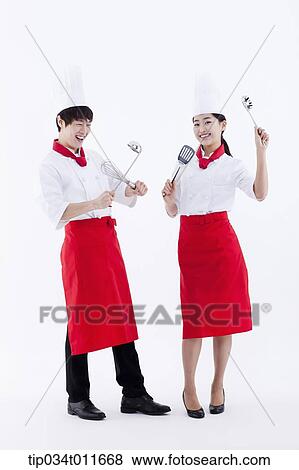 Stock Photo - female and male cook in red apron posing with kitchen utensils. Fotosearch