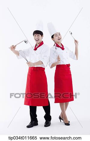 Stock Photography - female and male cook in red apron posing with kitchen utensils. Fotosearch