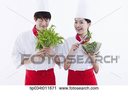 Stock Image - female and male cook in red apron with posing with salad. Fotosearch