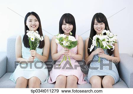 Stock Photo - ladies holding white flowers on a couch. Fotosearch