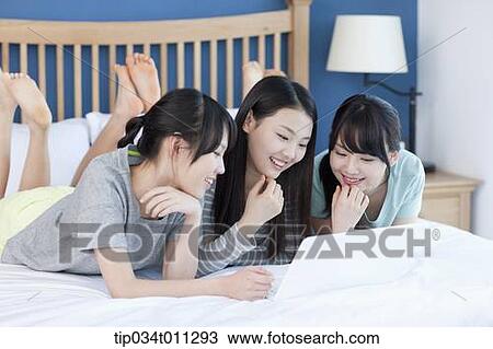 ladies sharing a laptop while lying on a bed View Large Photo Image Stock Image - ladies sharing a laptop while lying on a bed. Fotosearch