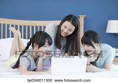 Stock Image - ladies sharing a laptop while lying on a bed. Fotosearch