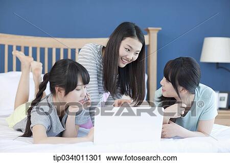 Stock Image - ladies sharing a laptop while lying on a bed. Fotosearch