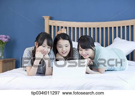 Stock Photo - ladies sharing a laptop while lying on a bed. Fotosearch