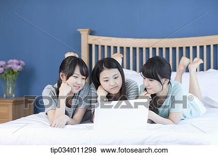 Stock Photo - ladies sharing a laptop while lying on a bed. Fotosearch