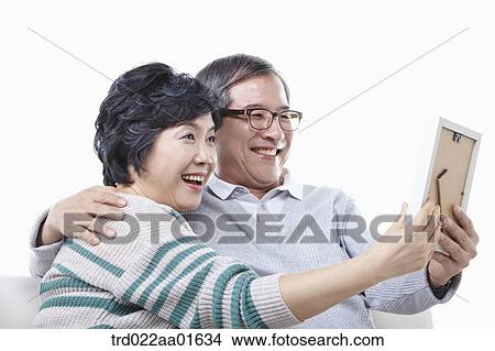 middle aged couple sitting on a couch with family photo album View Large Photo Image Picture - middle aged couple sitting on a couch with family photo album. Fotosearch