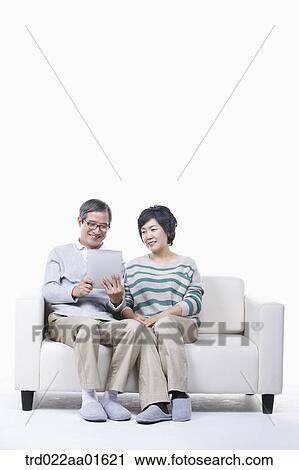 Stock Image - middle aged couple sitting on a couch sharing tablet PC. Fotosearch
