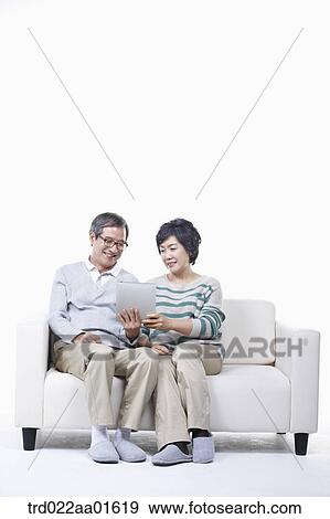 middle aged couple sitting on a couch sharing tablet PC View Large Photo Image Stock Photo - middle aged couple sitting on a couch sharing tablet PC. Fotosearch