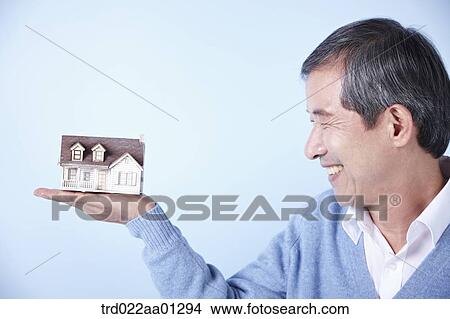 Picture - middle aged man holding a mini house on his hand. Fotosearch
