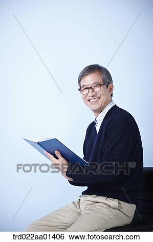 Stock Photograph - middle aged man reading a book while sitting on a chair. Fotosearch