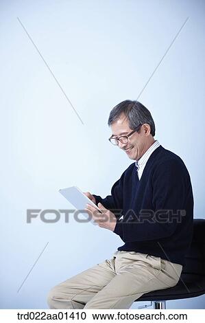 middle aged man using tablet PC while sitting on a chair View Large Photo Image Stock Image - middle aged man using tablet PC while sitting on a chair. Fotosearch