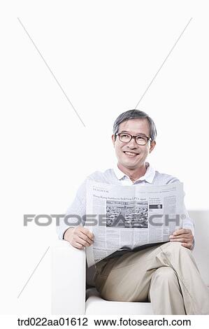 Stock Image - middle aged sitting on a couch reading a newspaper. Fotosearch
