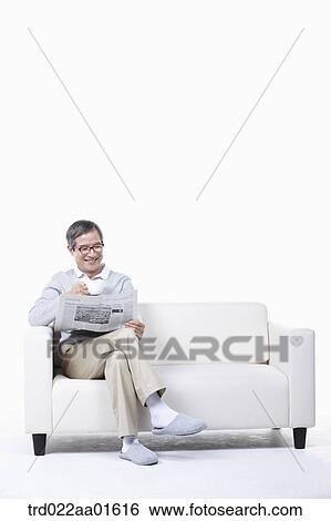 Stock Photograph - middle aged sitting on a couch reading a newspaper. Fotosearch