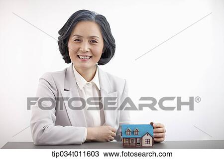 Stock Image - middle aged woman in business suit with a toy house. Fotosearch