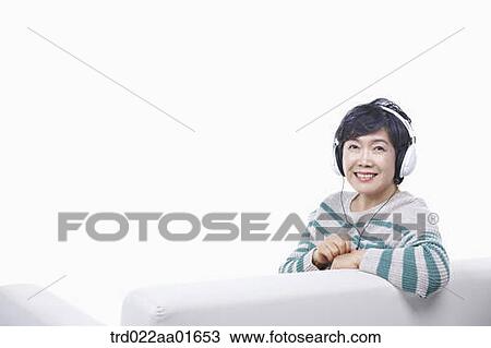 Stock Image - middle aged woman listening to music on a couch. Fotosearch
