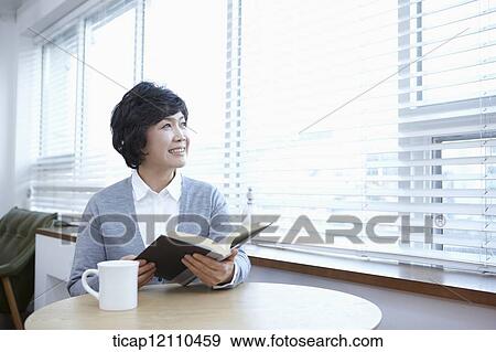 Stock Photo - middle aged woman reading a book sitting at table. Fotosearch