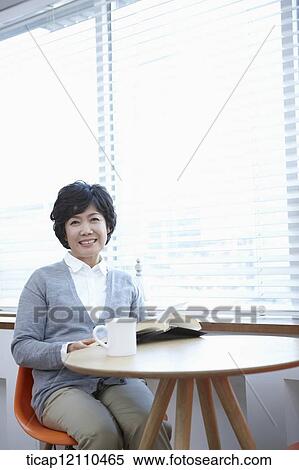 Stock Photography - middle aged woman reading a book sitting at table. Fotosearch
