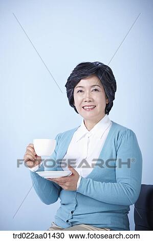 middle aged woman sitting on a chair drinking coffee View Large Photo Image Stock Image - middle aged woman sitting on a chair drinking coffee. Fotosearch