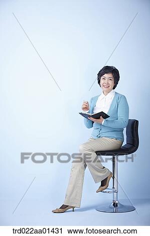 middle aged woman sitting on a chair with a pen and book View Large Photo Image Stock Image - middle aged woman sitting on a chair with a pen and book. Fotosearch