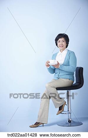 middle aged woman sitting on a chair drinking coffee View Large Photo Image Stock Photo - middle aged woman sitting on a chair drinking coffee. Fotosearch