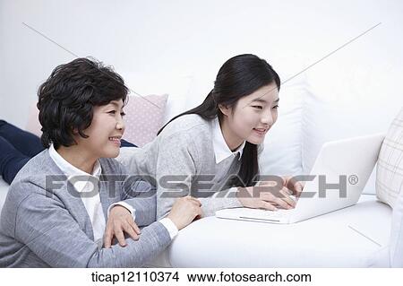 Picture - mother next to daughter using laptop on the bed. Fotosearch