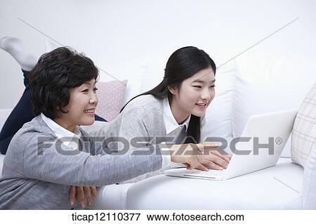 Stock Photo - mother next to daughter using laptop on the bed. Fotosearch