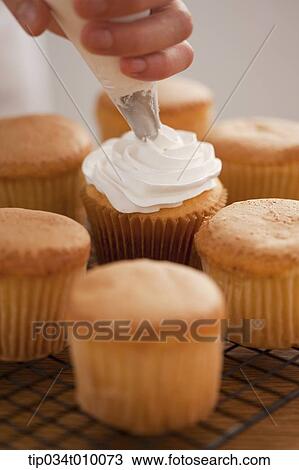 Stock Image - putting whip cream on cup cake. Fotosearch