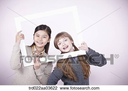 Stock Image - two girls with empty frame around themselves. Fotosearch