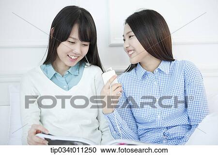 Stock Image - two ladies listening to music together. Fotosearch