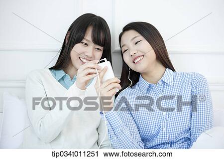 Stock Image - two ladies listening to music together. Fotosearch