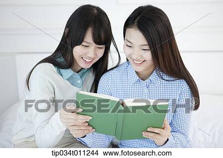 Picture - two ladies reading a book together. Fotosearch