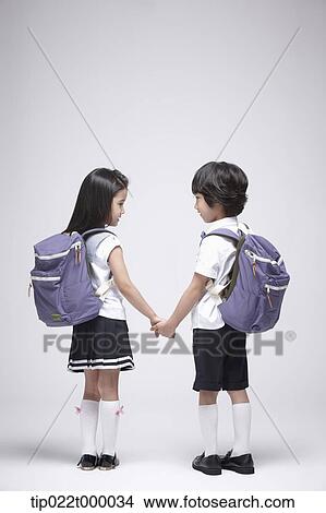 Picture - a boy and a girl wearing school bags holding hands. Fotosearch