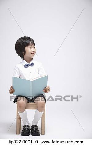 Stock Image - a boy sitting on a chair reading a book. Fotosearch