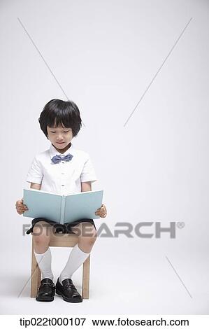 Stock Photo - a boy sitting on a chair reading a book. Fotosearch