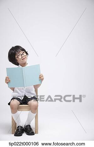a boy sitting on a chair reading a book View Large Photo Image Stock Photograph - a boy sitting on a chair reading a book. Fotosearch
