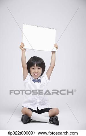 Stock Photo - a boy sitting on the floor holding a blank sketch book. Fotosearch