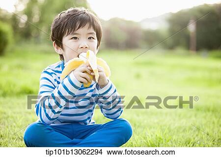 a boy sitting on the grass eating a banana View Large Photo Image Picture - a boy sitting on the grass eating a banana. Fotosearch
