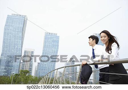 Stock Photograph - a business man and a business woman leaning on a fence. Fotosearch