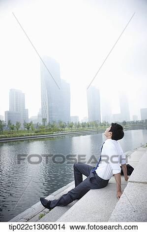 Picture - a business man sitting next to a river. Fotosearch