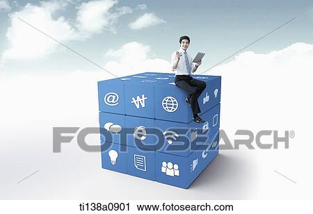Stock Image - a business man sitting on a cube with icons. Fotosearch