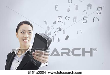 a businesswoman holding a mobile phone with icons flying View Large Photo Image Picture - a businesswoman holding a mobile phone with icons flying. Fotosearch