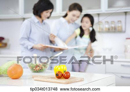 Stock Photo - a child reading a book with two women in the kitchen. Fotosearch