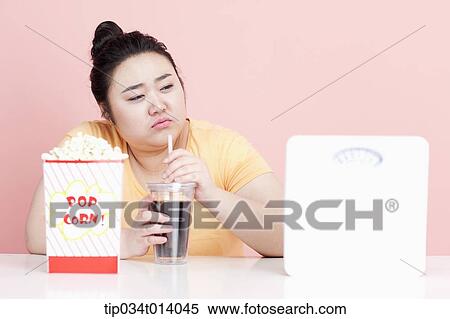 Stock Photography - a chubby woman drinking a coke with popcorn in front of her. Fotosearch