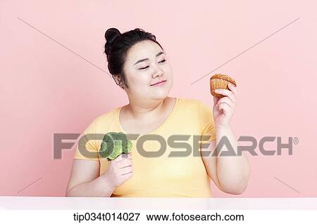 a chubby woman holding broccoli and cupcake View Large Photo Image Stock Photo - a chubby woman holding broccoli and cupcake. Fotosearch