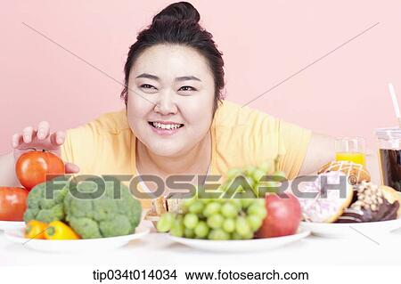 Picture - a chubby woman with plates full of food in front of her. Fotosearch