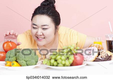 Stock Image - a chubby woman with plates full of food in front of her. Fotosearch