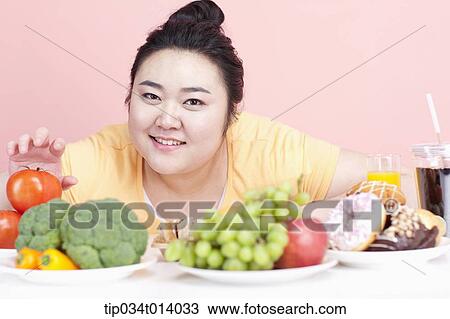 Stock Image - a chubby woman with plates full of food in front of her. Fotosearch