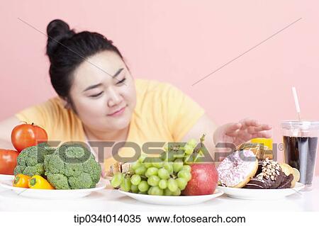 Stock Photography - a chubby woman with plates full of food in front of her. Fotosearch