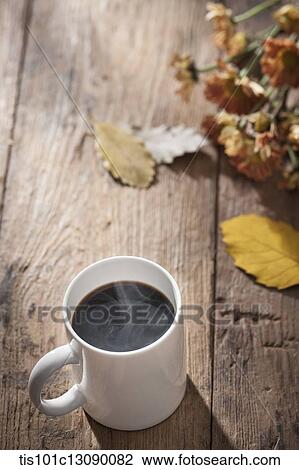 Stock Image - a cup of coffee on wooden surface with autumn flowers. Fotosearch