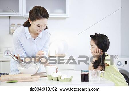 Stock Image - a daughter watching mother cooking. Fotosearch